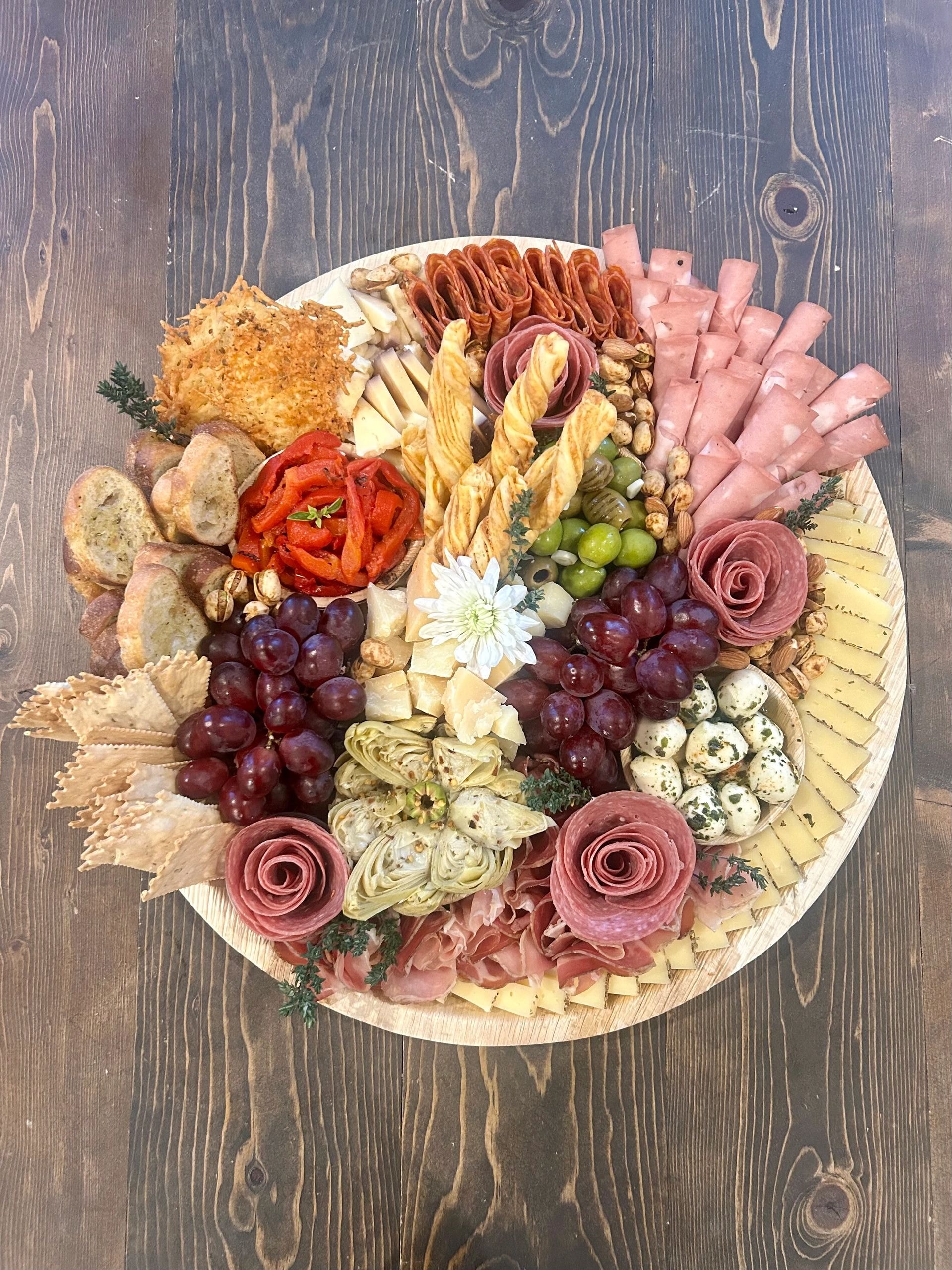 Large round charcuterie board with artichokes and salami roses